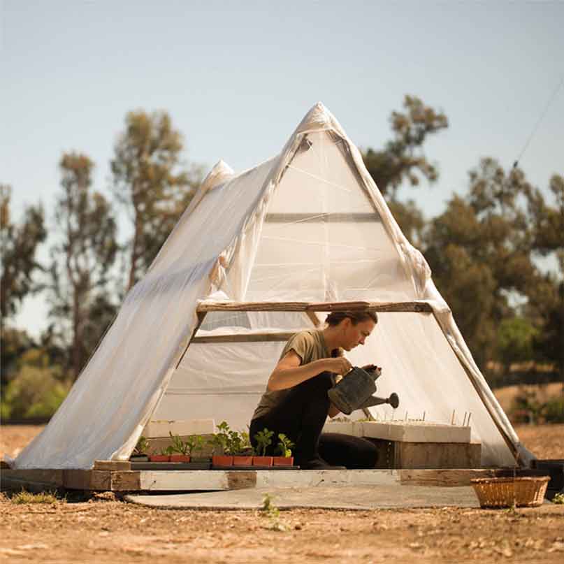 girl in "greenhouse" tent watering plants